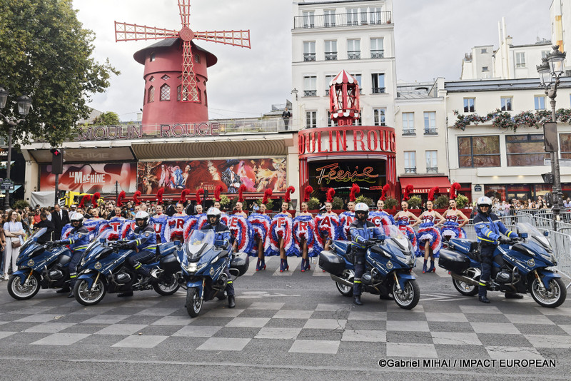 Des gendarmes motocyclistes de l'escorte officielle du Tour de France prennent position devant les danseuses du Moulin Rouge, place Blanche à Paris.